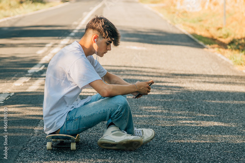 teenage boy with mobile phone and skateboard on the road