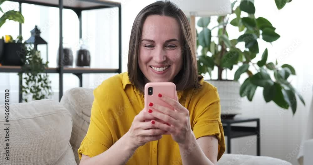 Happy woman text messaging using mobile phone while drinking coffee on sofa at home Happy woman text messaging using mobile phone while drinking coffee on sofa at home