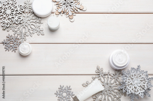 Flat lay composition with cosmetic products and snowflakes on white wooden table, space for text. Winter skin care
