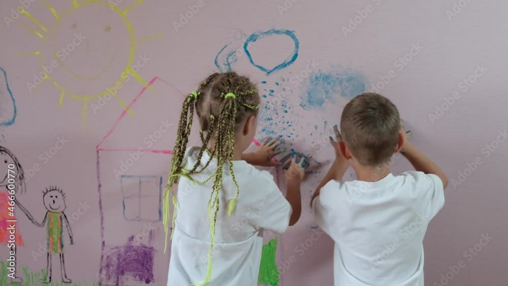A little girl and a boy preschoolers paint with their hands on a wall ...