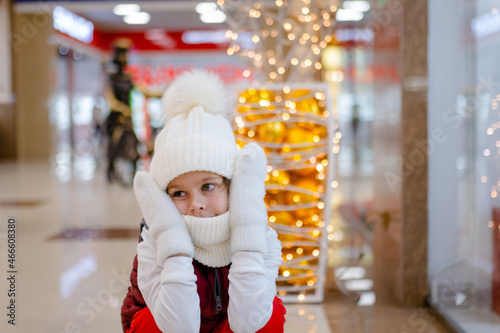 surprised boy in white bobble hat and scarf at mall near showcase. blurred bright lights on background © habrovich