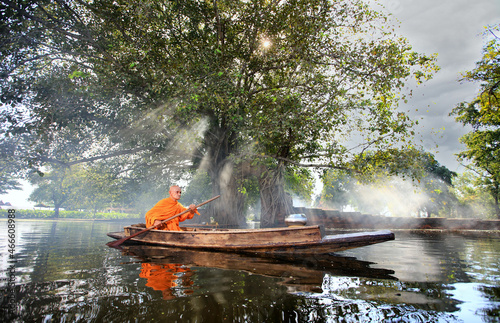 Unseen elderly monk boating pass ruins temple and Bodhi Tree to get food offering
