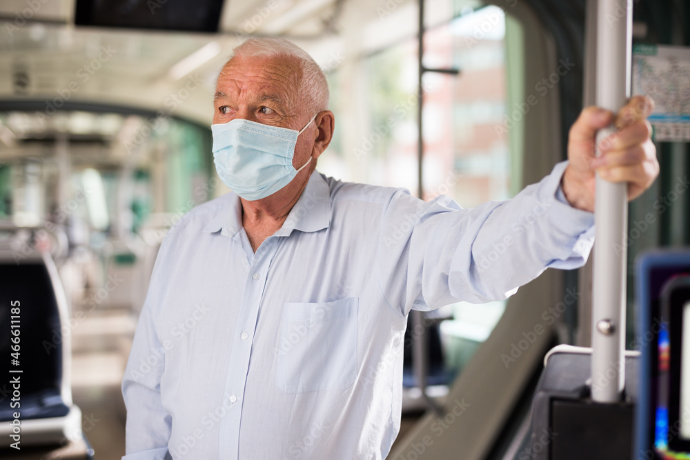 Old European man in face mask standing in streetcar and waiting for next stop.