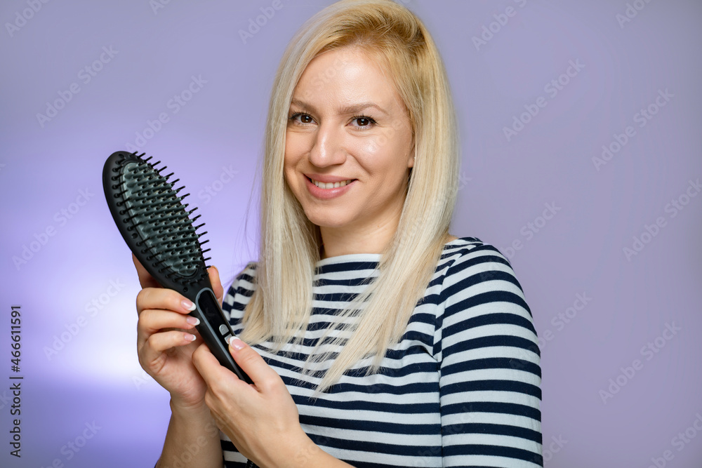 Woman in her thirties with blonde hair holding electric comb and smiling Woman in her thirties with blonde hair holding electric comb and smiling