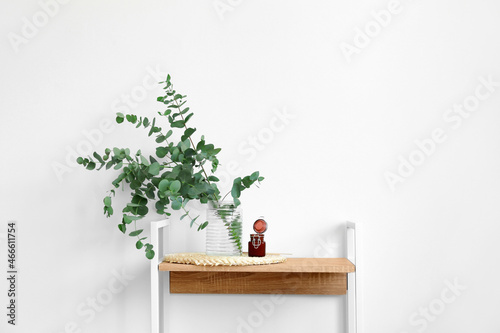 Fototapeta Naklejka Na Ścianę i Meble -  Vase with green eucalyptus branches and candle on shelf near white wall