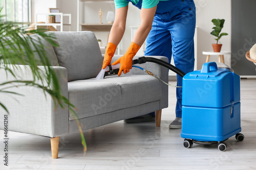 Fotografie Male worker removing dirty stain from grey sofa with vacuum cleaner in room