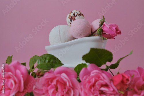 Bath bombs with rose extract in a ceramic bath and pink roses on a pink background.Pink bath bombs and pink rose flowers- Flower Bath Bombs.Beauty and aromatherapy. Organic vegan eco cosmetics.