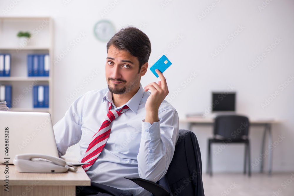 Young male employee holding credit card at workplace Young male employee holding credit card at workplace