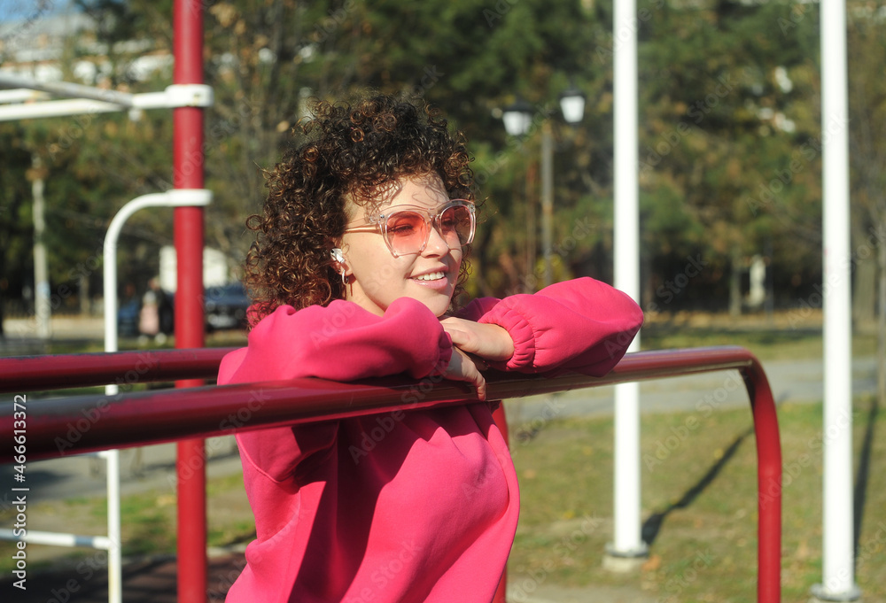 Obraz premium Cute curly hair woman in pink sportswear with headphones on the playground