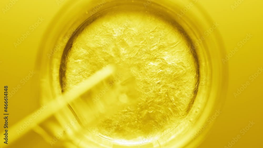 Top view macro shot of glycerin pouring into beaker with water creates ripples on its surface on yellow background | Abstract body care cosmetics formulation concept