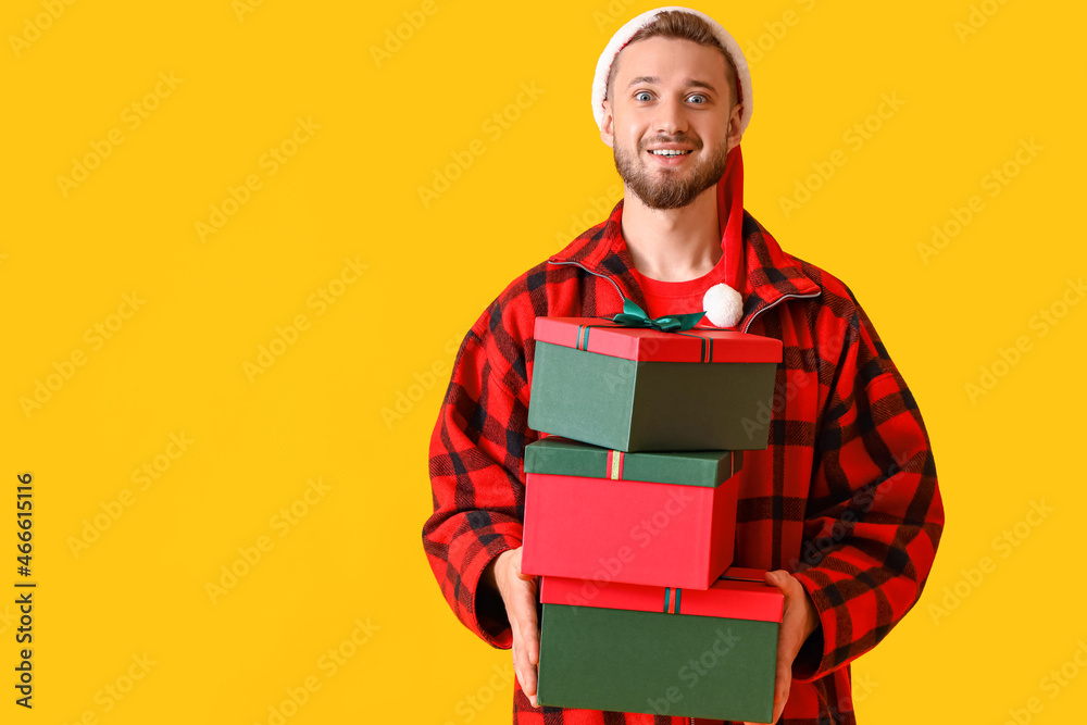Young man in Santa hat with Christmas gifts on yellow background Young man in Santa hat with Christmas gifts on yellow background