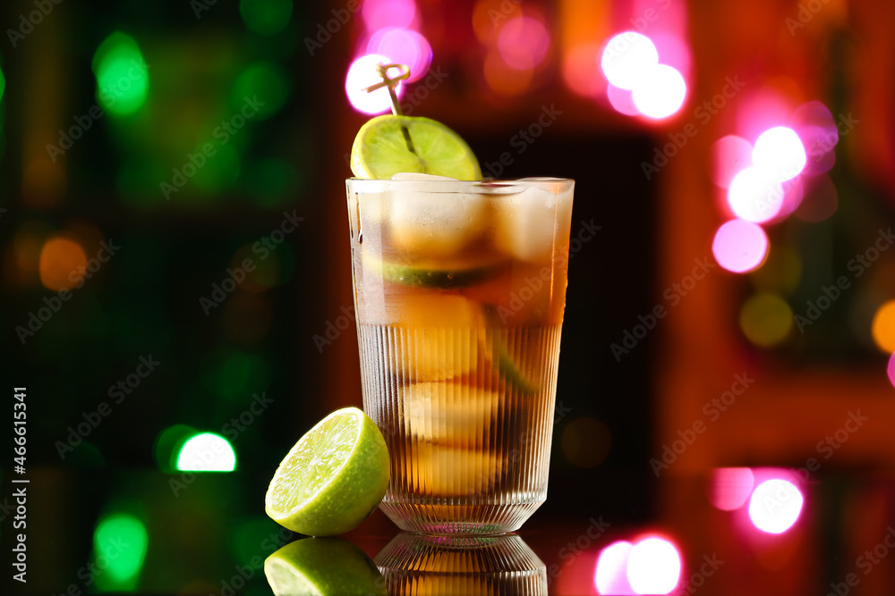 Glass of tasty Cuba Libre cocktail on table against blurred lights Glass of tasty Cuba Libre cocktail on table against blurred lights