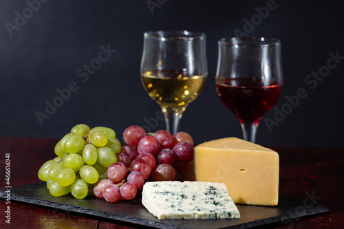 Wine  cheese  some grapes and pear on wooden plate on black background