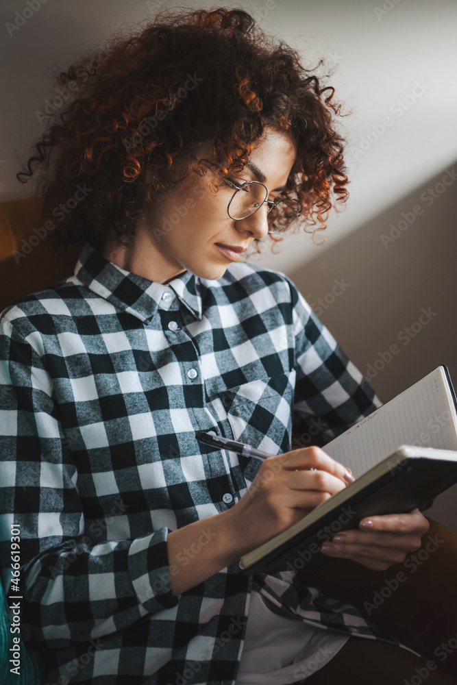 Curly woman notes something in her notebook. Planning the day. Home isolation Curly woman notes something in her notebook. Planning the day. Home isolation