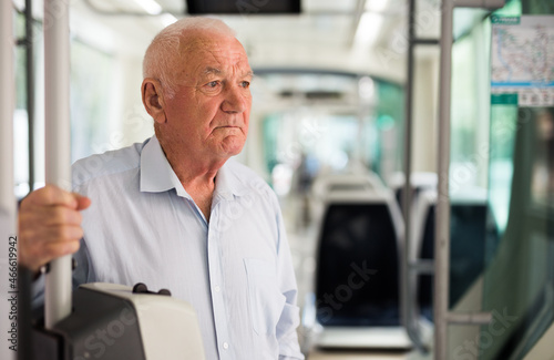 Senior European man standing inside tram and waiting for his stop.
