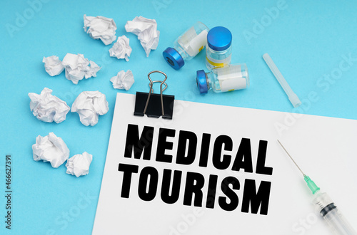 On a blue background, a syringe, medicine, crumpled pieces of paper and a sheet with the inscription - MEDICAL TOURISM