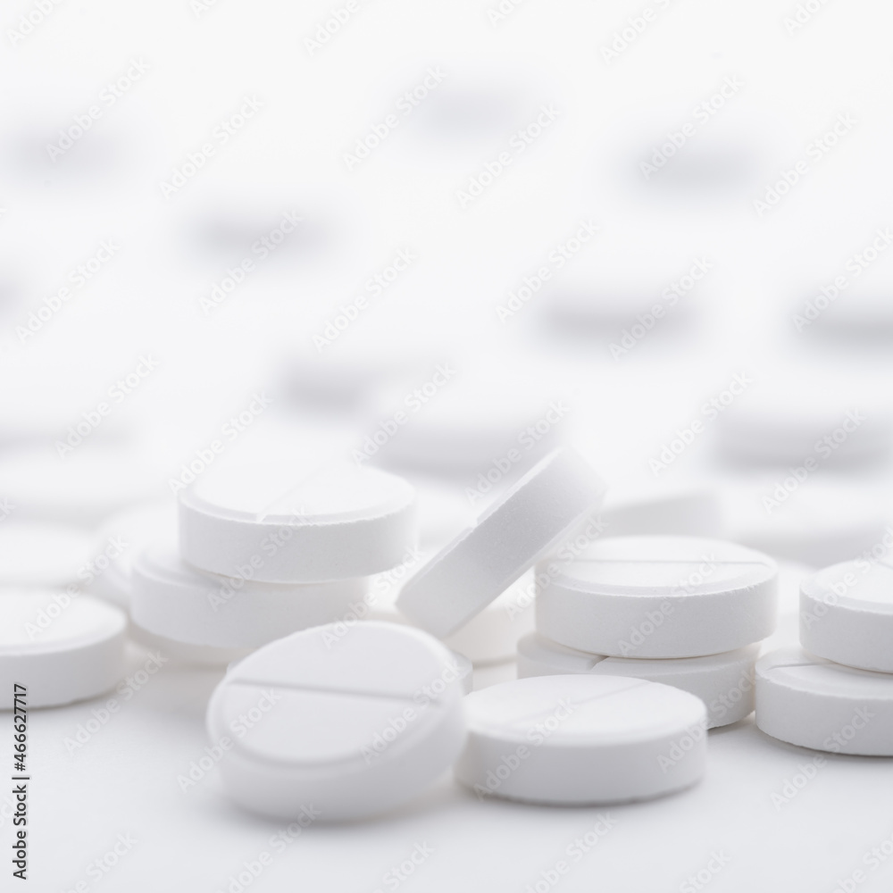 A pile of white pills scattered on a bright white background. Selective focus. A pile of white pills scattered on a bright white background. Selective focus.