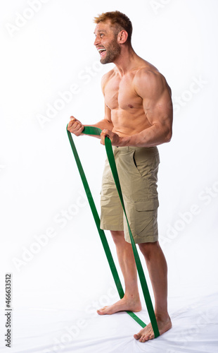 muscular man in shorts shakes muscles or poses with an elastic band for fitness. grey background