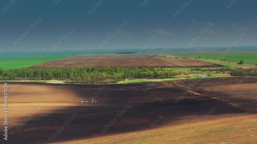 4K Aerial Elevated View. Red Tractor Plowing Field. Beginning Of Agricultural Spring Season. Cultivator Pulled By A Tractor In Countryside Rural Field Landscape. Flight Above And Around.