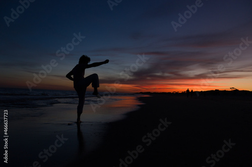 silueta de hombre practicando artes marciales al atardecer en la playa