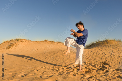 joven practicando artes marciales al atardecer sobre dunas de arena, saltando  © Galdys V
