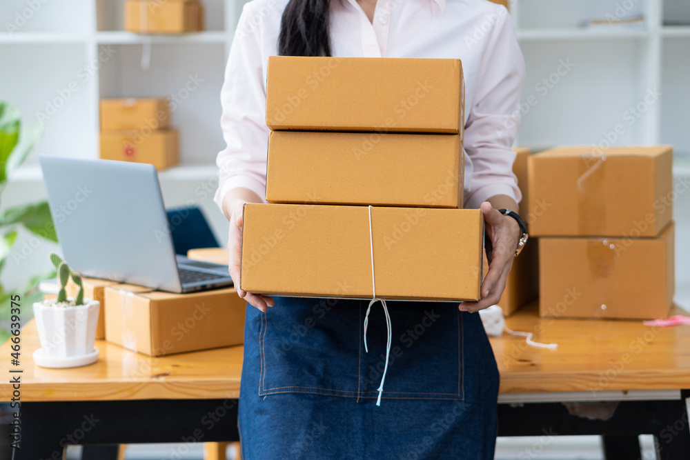 Small business, SME, freelance, a young woman working at the home portrait with box, smartphone, laptop, online, marketing, packaging, shipping, SME, e-commerce, and delivery concept. Small business, SME, freelance, a young woman working at the home portrait with box, smartphone, laptop, online, marketing, packaging, shipping, SME, e-commerce, and delivery concept.