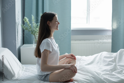A beautiful teenager wakes up in the morning, bright light on her from a large window. Happy teenage girl meets a new day in a beautiful room. 