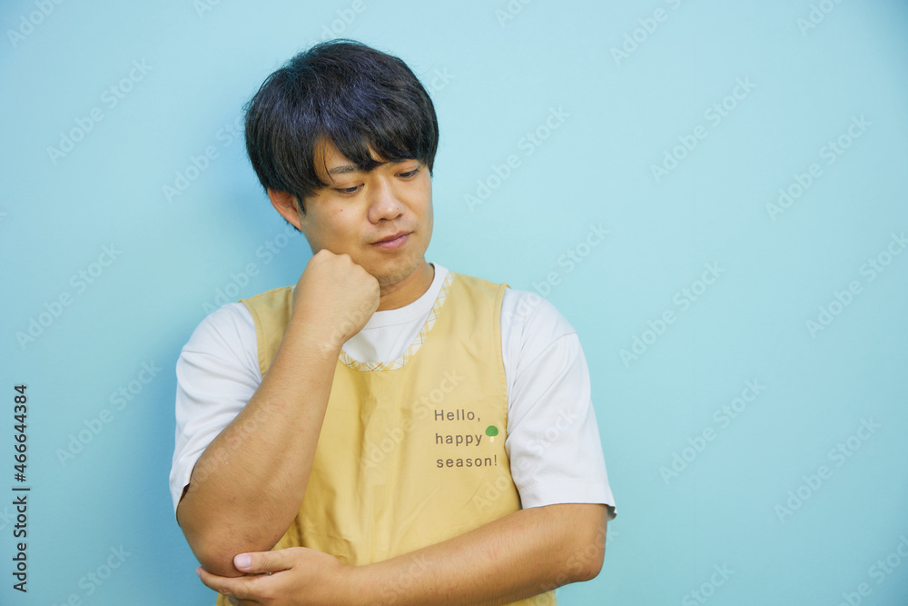 困った様子で考えるエプロンを付けたアジア人男性