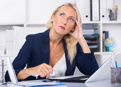 Obraz na płótnie Portrait of worried mature female manager working on laptop in office