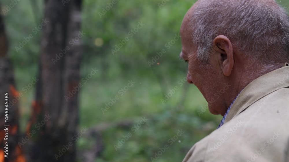 An old man sitting alone by the fire is sad. A male tourist is on vacation in the wild
