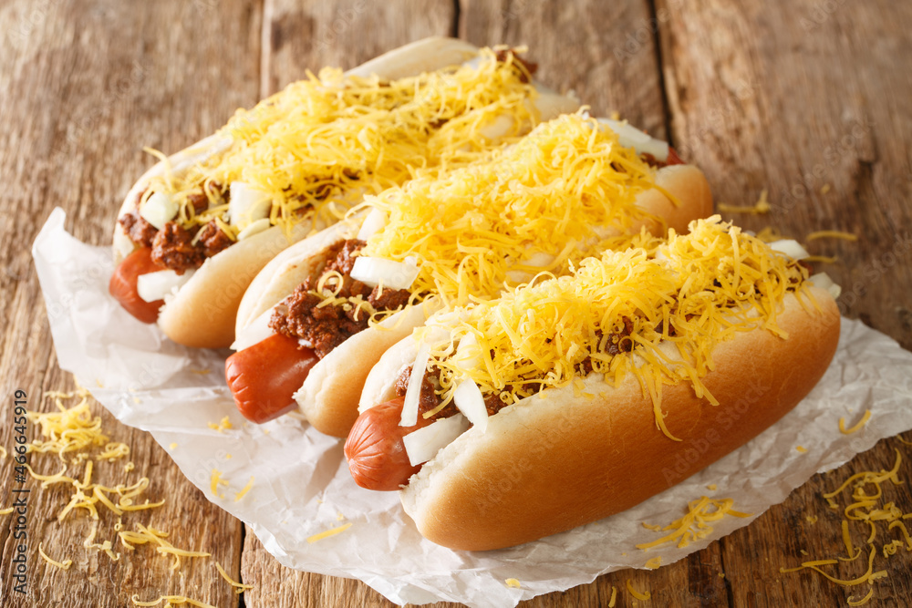 American chili hot dog with beef sausage, cheddar cheese and onions close-up on an old wooden background. horizontal