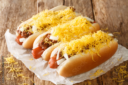 American chili hot dog with beef sausage, cheddar cheese and onions close-up on an old wooden background. horizontal photo