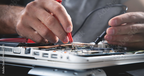 Technician hands checking motherboard with multimeter.