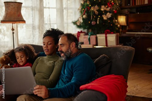 Diverse parents and daughter using tablet on sofa at home