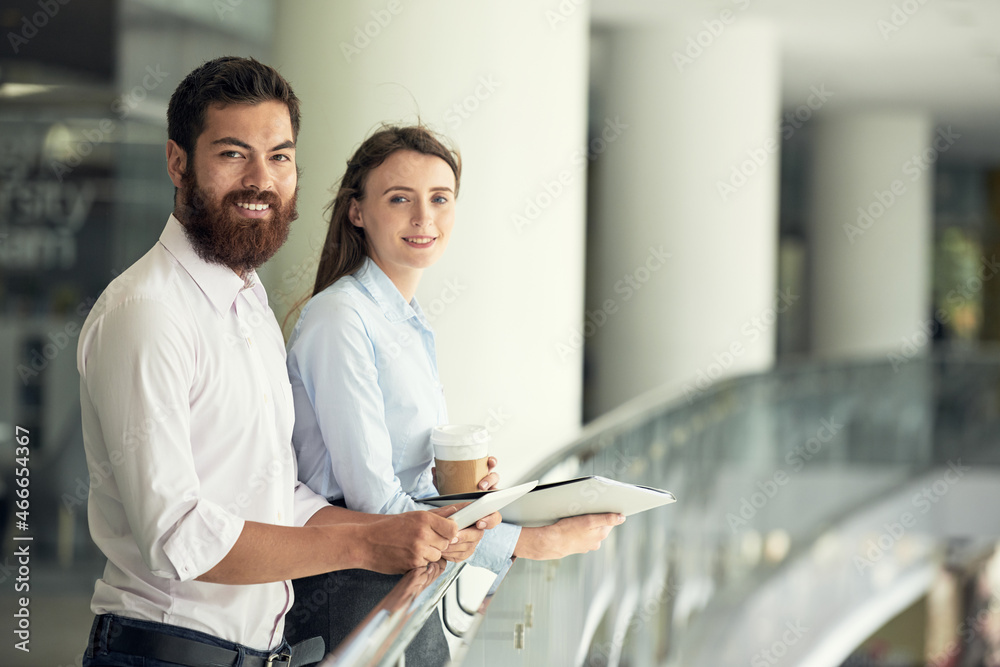 Portrait of smiling successful young business people in shirts standing at railing in modern office