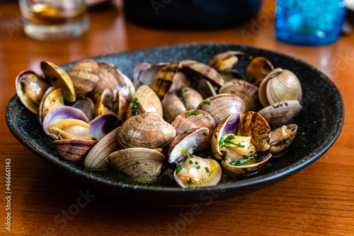 Cooked clams on black ceramic plate on wooden table of restaurant. Traditional asturian food photo