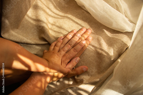Hands of parents and child on a background of brown fabric with sunlight. Family and support concept. Top view