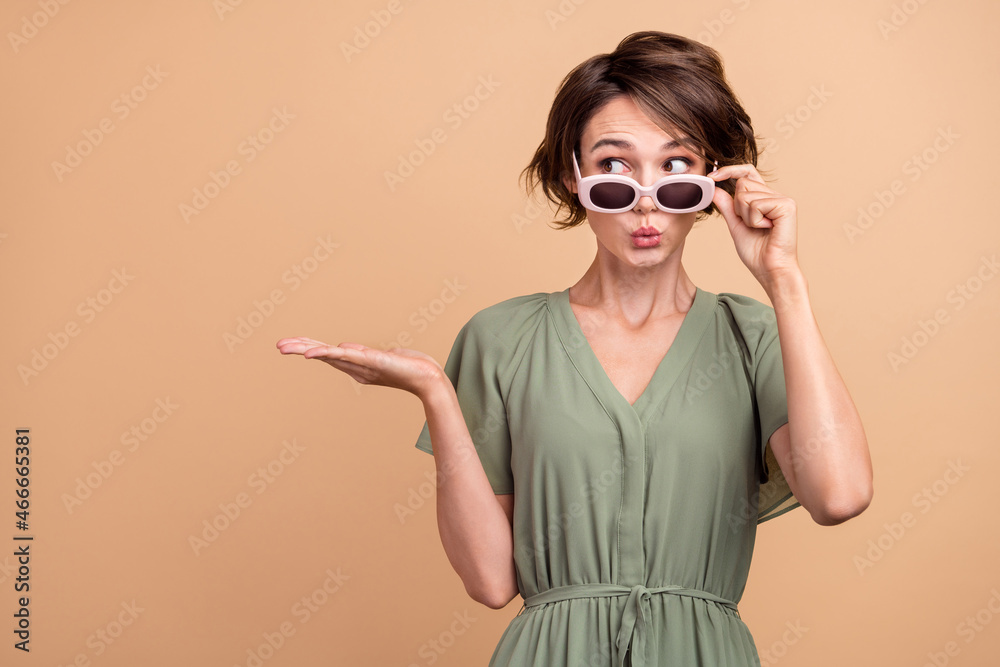 Photo of dreamy shocked happy young woman hand empty space object wear sunglass news isolated on beige color background Photo of dreamy shocked happy young woman hand empty space object wear sunglass news isolated on beige color background