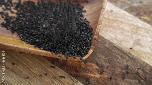 Black sesame seeds on a rustic wooden surface. Falling in slow motion. Close up. Organic healthy whole grain seasoning photo