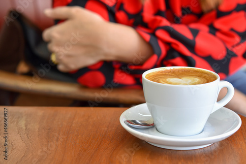 Warm white coffee cup on wooden table with blurred woman hand.