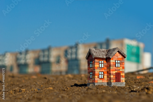 Brick toy house on the ground. Orange house on a background of high-rises. The concept of own housing and construction.
