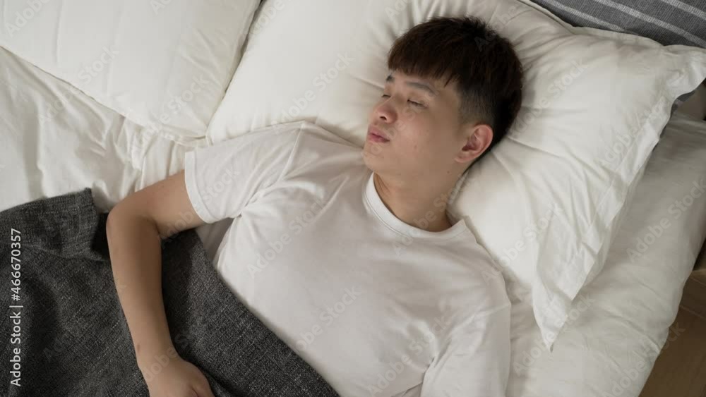 top shot with dutch angle asian young male waking up naturally from sound sleep is lying in bed and looking away into distance with a smile on a good day at home top shot with dutch angle asian young male waking up naturally from sound sleep is lying in bed and looking away into distance with a smile on a good day at home