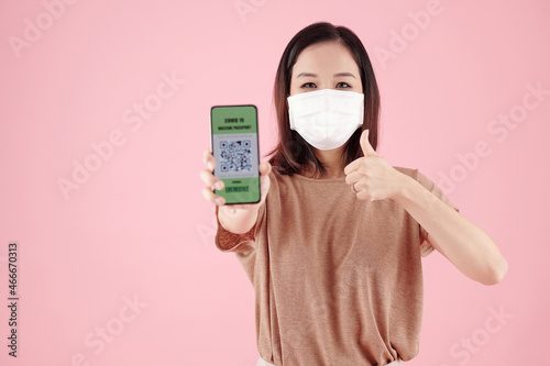 Young man holding smartphone with QR code on the screen that links to COVID 19 vaccination passport