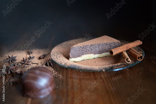 one piece of chocolate cheesecake on a transparent plate decorated with cinnamon, candy and cloves on a wooden background. Close-up, in dark tones