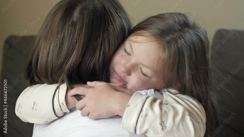 Waking up little girl in pajamas happily hugs her mother.