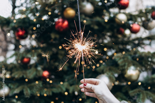 A burning Christmas fire in the hands of a modern woman on the background of a Christmas tree. Christmas, New Year