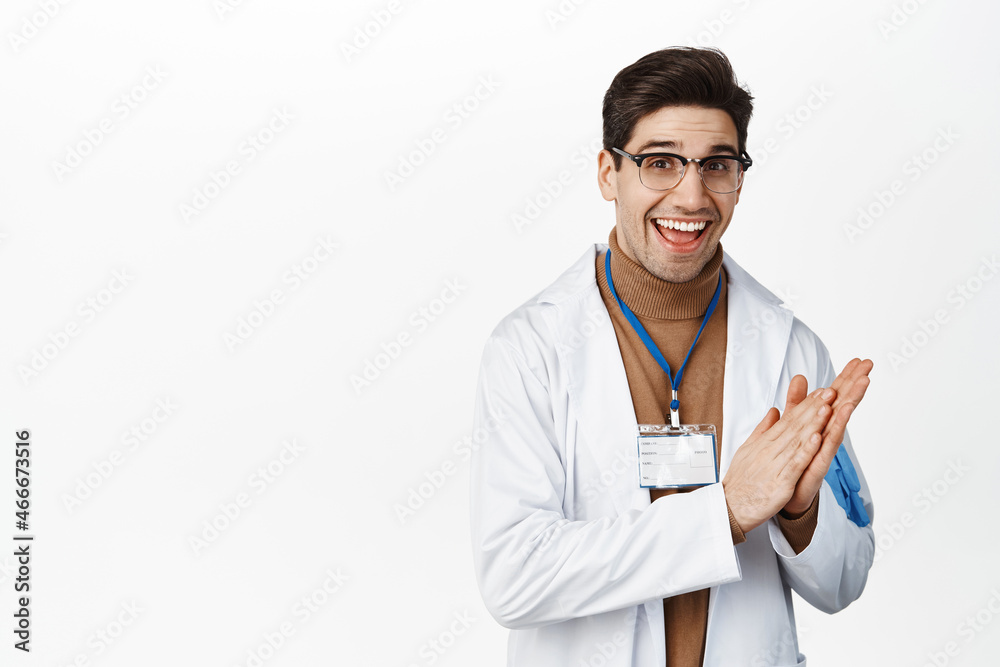 Happy smiling doctor clapping hands, applause and look pleased, standing in medical robe and glasses against white background Happy smiling doctor clapping hands, applause and look pleased, standing in medical robe and glasses against white background