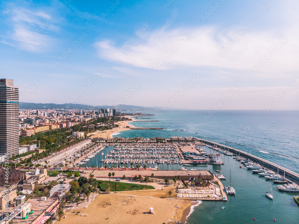 Drone shot Barcelona. Port with boats near the coast. Drone view of a vibrant swimming and sunbathing beach in Barcelona. People are relaxing on the beach. Panoramic view of the city of Barcelona. 
