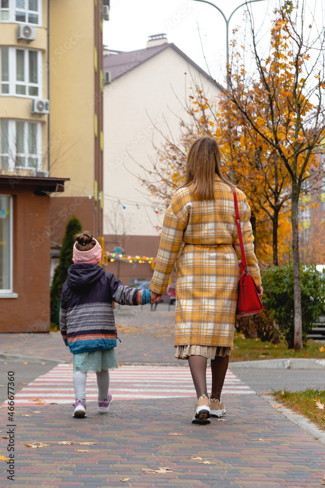 Mother walking with daughter on autumn street. Fall colors