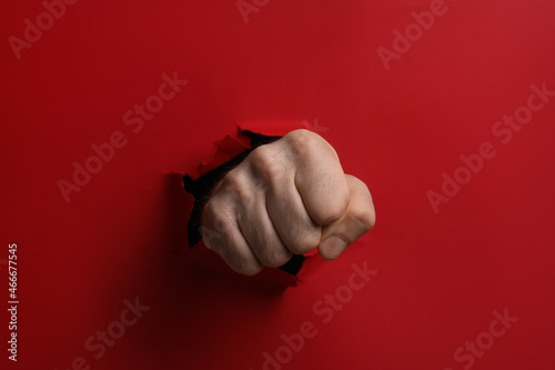 Man breaking through red paper with fist, closeup